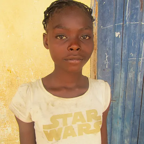 Jente i gul genser står foran vegg i Kamerun.