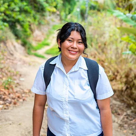 Jente med skolesekk går på grusevei i El Salvador.