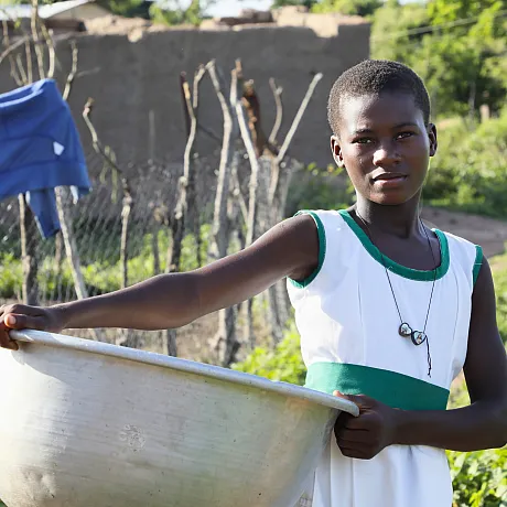 Jente i Ghana bærer en bøtte på en åker.