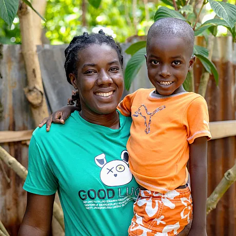 Mor løfter opp sin sønn i Haiti, begge ser i kameraet.