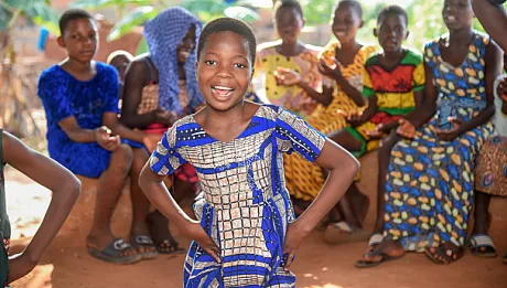 Jente i mønstret blå kjole danser med barn i bakgrunnen.