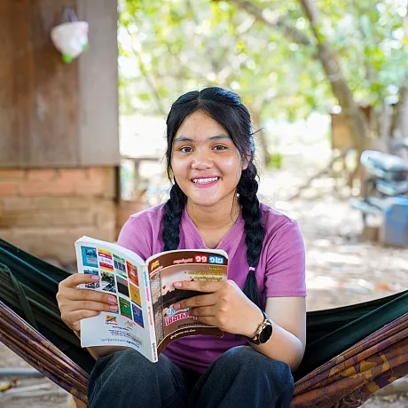 Jente i Kambodsja leser avis i hengematte.