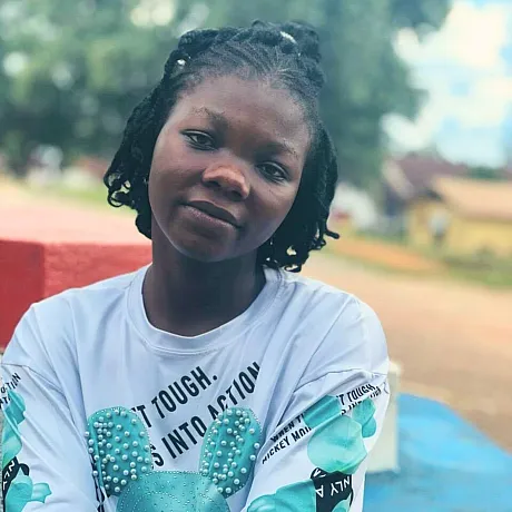 Jente i Liberia med hvit genser sitter utendørs og ser inn i kameraet.