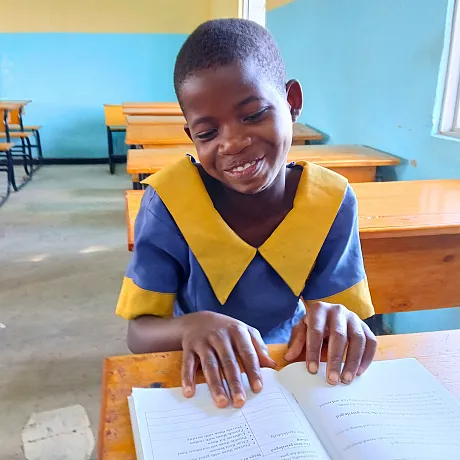 Jente i Malawi leser i notatboken sin i et klasserom.