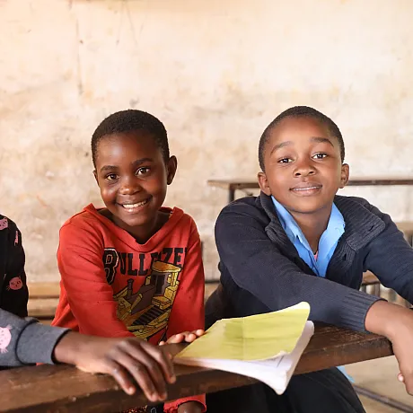 Tre barn sitter i klasserom i Malawi