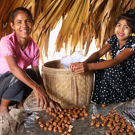 Mor og datter sitter på gulvet med kastanjer og smiler mot kameraet.