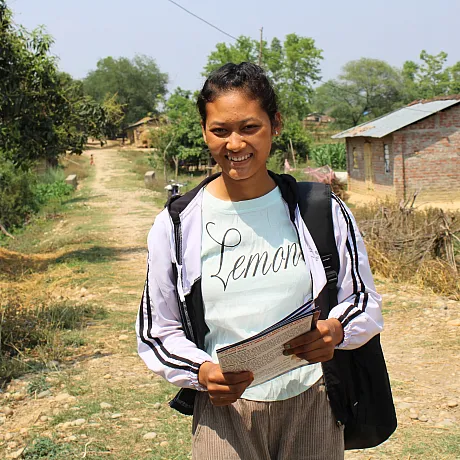 Jente i Nepal står på en vei med en notatbok.