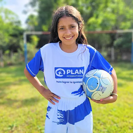 Jente i Paraguay poserer på plenen med fotball og fotballdrakt.