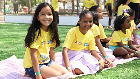 Jenter som sitter på gresset og smiler mot kameraet.