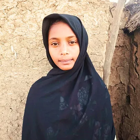 Jente i Sudan står foran huset sitt.