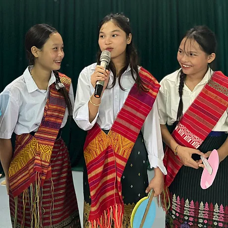 Tre jenter, en har mikrofon og snakker forran folk.